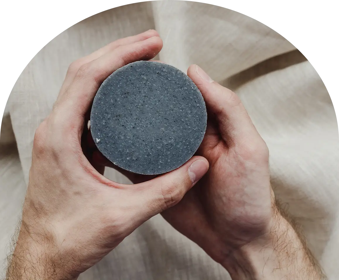 Hands holding a round gray soap bar.